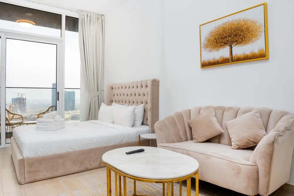 Studio living and sleeping area with sofa, marble-top table, and balcony city view