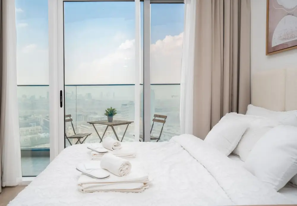 White bedding and fresh towels beside the balcony with open city views