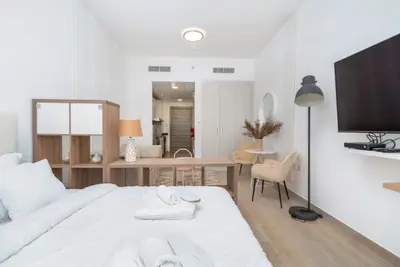 Studio seen from the bed with wall-mounted TV, desk and kitchen beyond