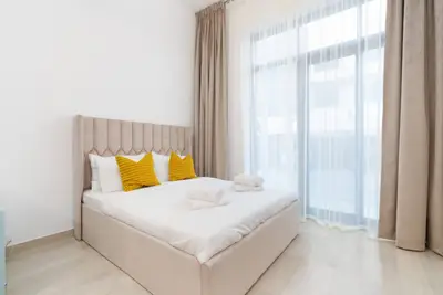 Double bed with mustard cushions beside floor-to-ceiling curtains