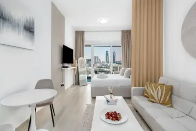 Open-plan living space with white corner sofa, TV and bed by the window