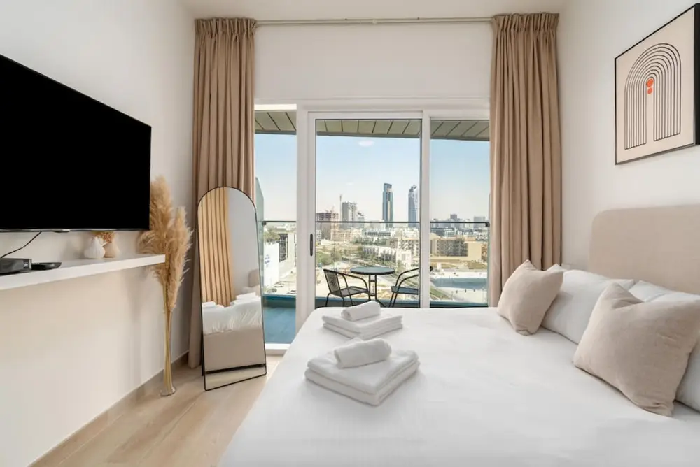 The bed faces a large TV, with balcony doors framing the skyline