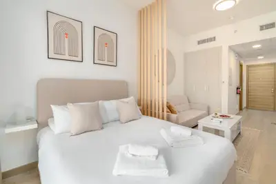 Bright studio bedroom with plush bed, slatted wood divider and sofa