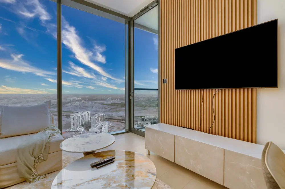 Living area with wall-mounted TV on a wood-slat panel and city view through corner glass