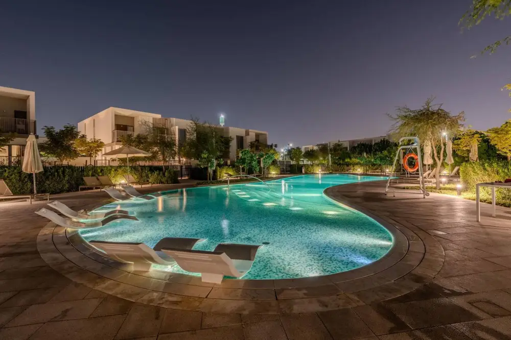 Resort-style community pool glowing at night with in-water loungers