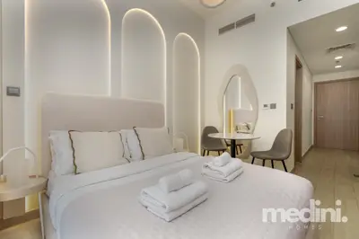 Bed with fresh towels, arch-lit wall and round mirror visible beyond the headboard