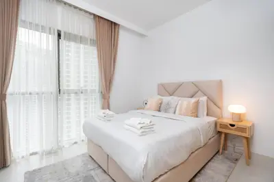 Restful double bed dressed in white beside a sunlit curtained window