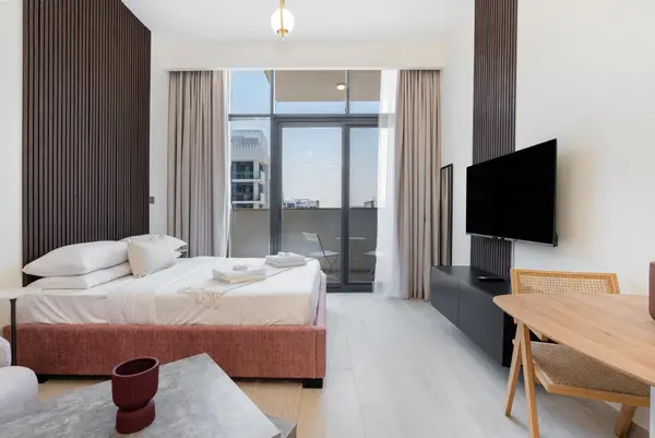 Studio overview with bed, large TV, dining set, and balcony door