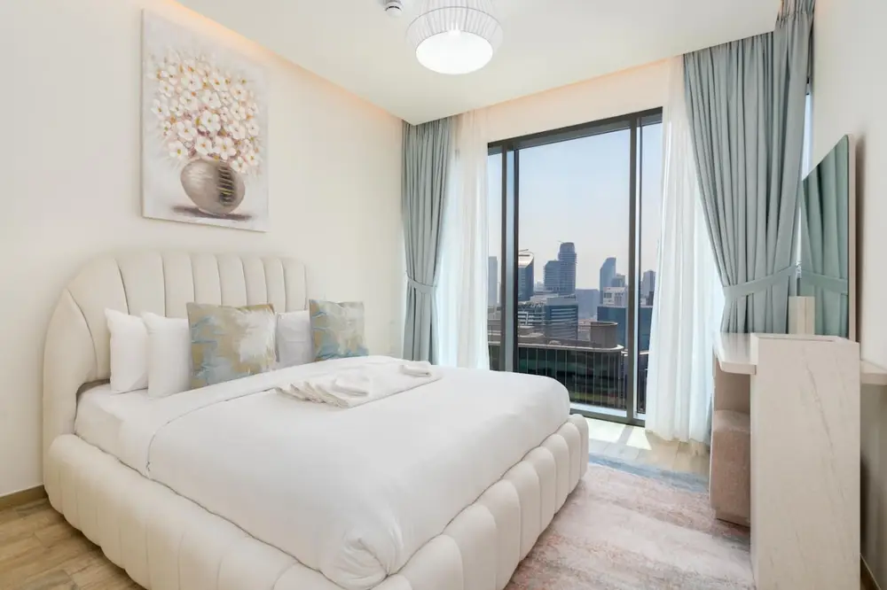 Bedroom with plush bed, floral artwork and city views through full-height windows