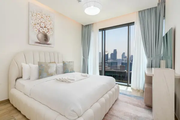 Bedroom with plush bed, floral artwork and city views through full-height windows