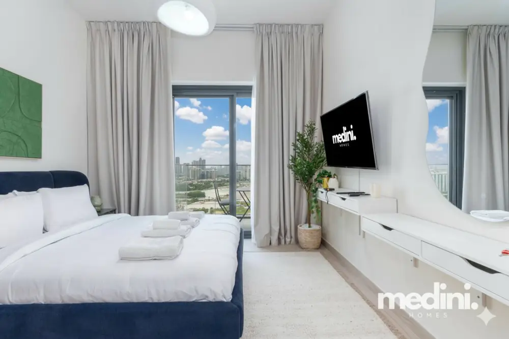 Studio bedroom with navy bed, wall TV and balcony views beyond