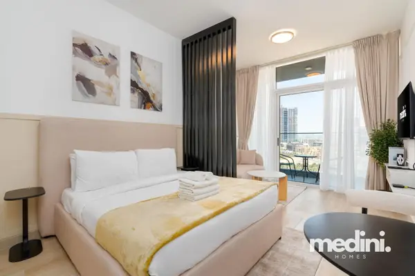 Studio bedroom with plush double bed and city views past the balcony curtains