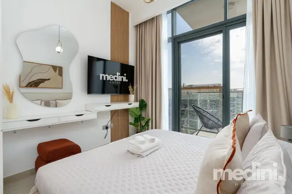 The bed beside a vanity mirror, TV and sunny balcony window