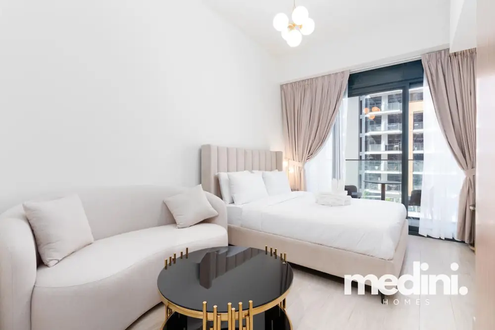 Bright studio with curved cream sofa, plush bed and round coffee table