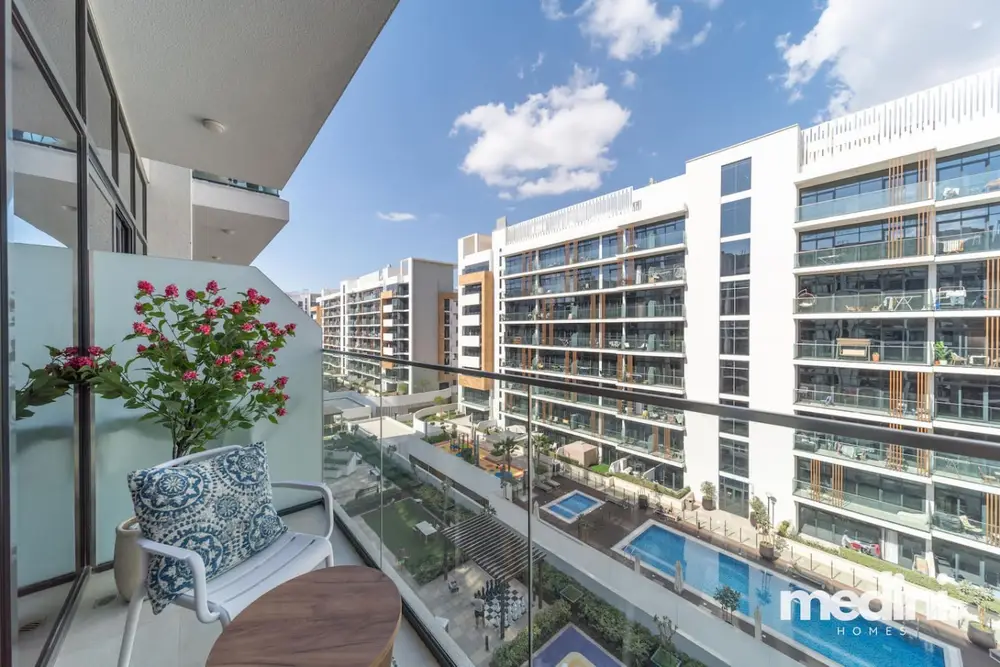 Balcony with two lounge chairs and a table, pool and towers in the background