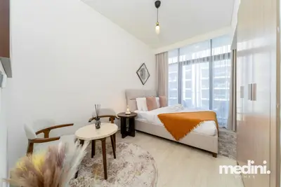 Bedroom with a double bed, orange throw, and tall window facing the complex