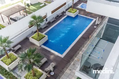Rooftop pool seen from above with lounge chairs, palm trees, and white facades