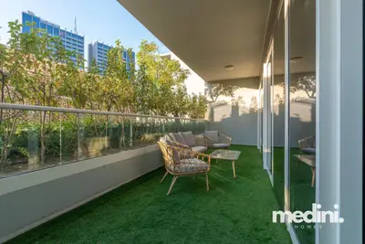Garden terrace with an artificial grass lawn, rattan chairs, and trees beyond the railing