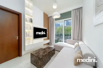 Living room with a large TV on built-in shelving, corner sofa, and balcony door