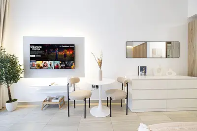 Living area with wall-mounted TV, round dining table and two textured chairs