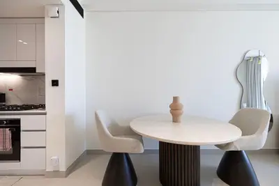 Dining area with round travertine-top table, two sculpted chairs and open kitchen