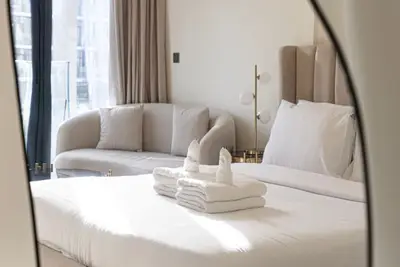 Mirror reflection of the bedroom showing bed with folded towels and a beige sofa