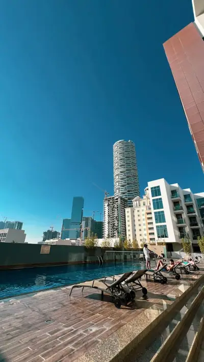 Outdoor rooftop pool with sun loungers and a tall residential tower beyond