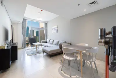 Open-plan living and dining area with sofa, TV, dining set, and floor-to-ceiling window