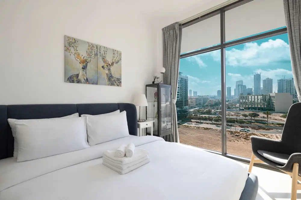Bedroom with white bed and a wide city-skyline view through a large window