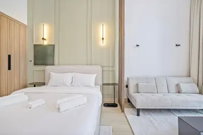 Crisp white bedding beside a sofa bed, framed by soft sage wall panelling