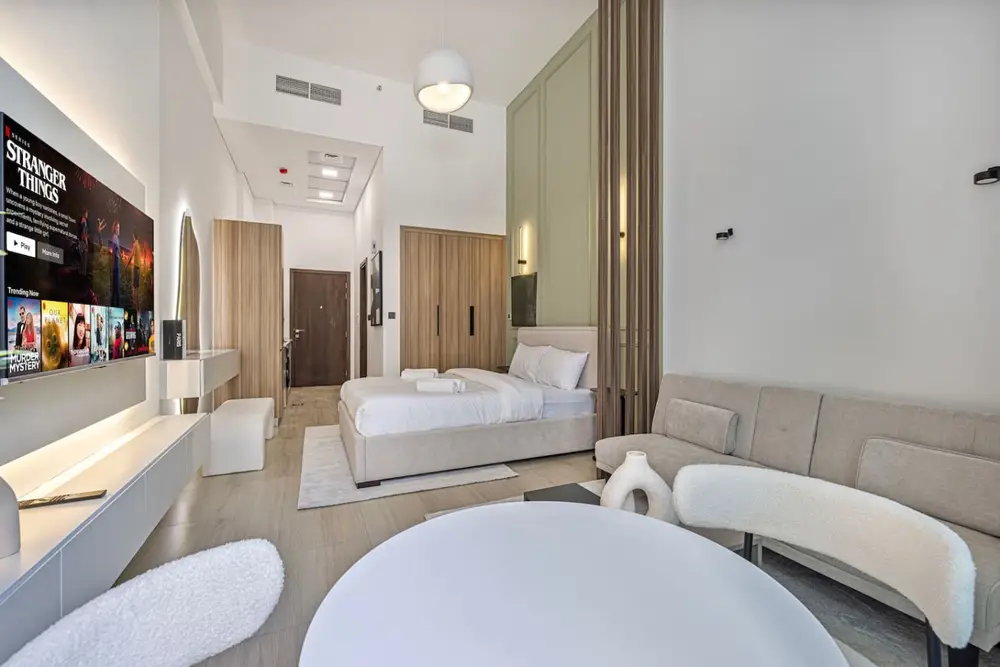 High-ceiling studio with a plush bed, wall TV and a soft seating corner