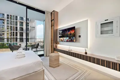 Bed with folded towels, backlit TV unit and a large glass door opening to the balcony