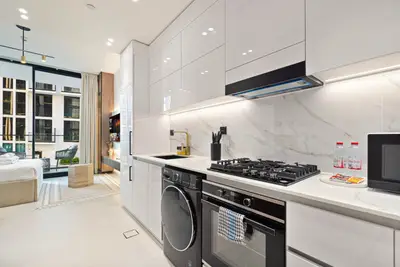 Kitchen with white gloss cabinets, gas hob and washing machine, living area beyond
