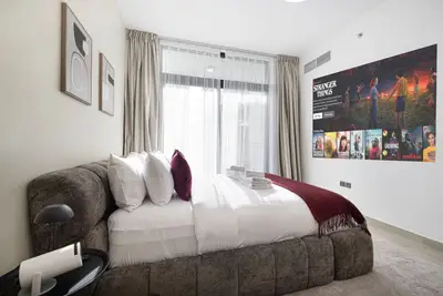 Bedroom with bouclé headboard, burgundy cushions, and TV on wall