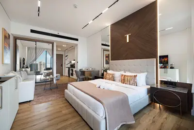Studio seen from the bed toward the sofa and kitchen corridor with wood panel accent wall