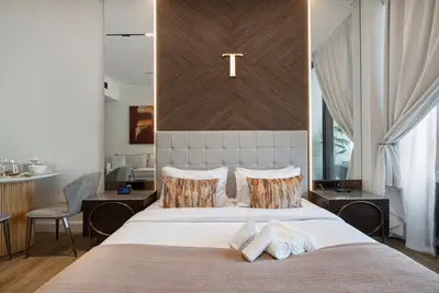Double bed with tufted headboard, patterned cushions and fresh towels laid out