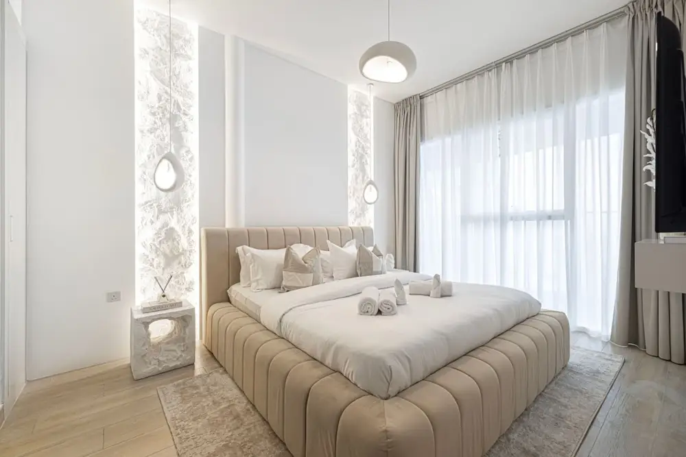 Bedroom with channelled velvet headboard, stacked pillows and sheer curtained window