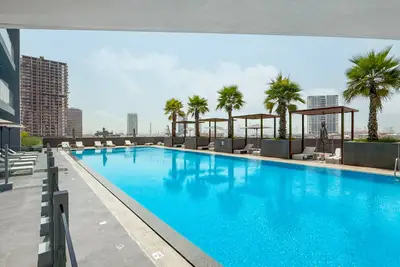 Rooftop swimming pool with sun loungers, palm trees and city skyline in the background