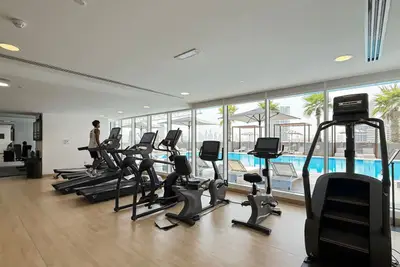 Gym with treadmills, exercise bikes and a view through glass onto the pool