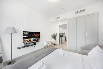 Studio angle showing the bed, wall-mounted TV, wardrobe, and kitchen beyond
