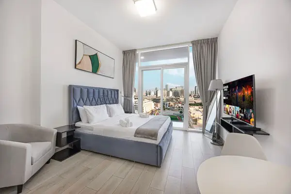 Bedroom with blue upholstered headboard, smart TV, and city views from the window