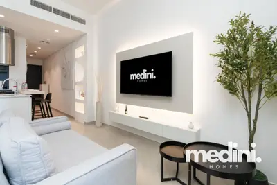 Living area with large TV on a backlit white panel, gray sofa, and side tables