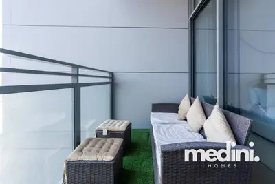 Balcony with rattan sofa set, cushions, artificial grass, and glass railing