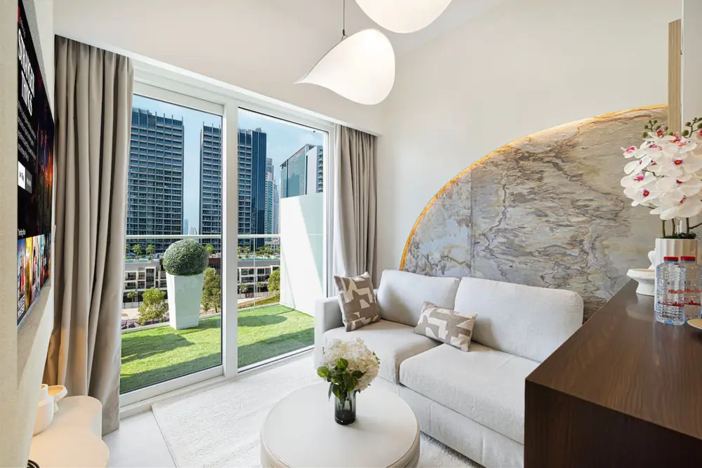 Living room with a sofa, round coffee table and balcony doors opening to a city view