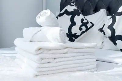 Stack of folded white towels on the bed beside patterned cushions and the tufted headboard