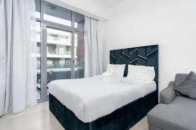 Double bed with dark velvet headboard beside a glass balcony door