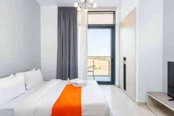 Bed with white linens and orange throw runner facing a large glazed balcony door