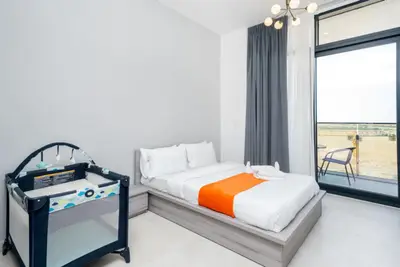 Bedroom with double bed, orange runner, baby cot, and floor-to-ceiling balcony door
