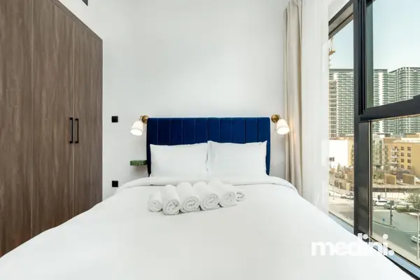 Bedroom with blue velvet headboard, wall sconces, and city view window