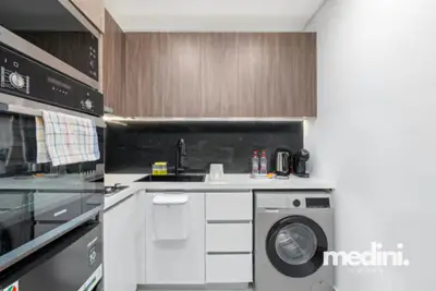 Compact kitchen with oven, washing machine, and dark tile splashback
